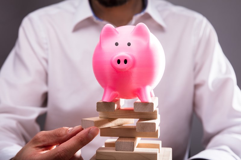 A pink plastic pig on top of wooden Jenga blocks in front of a man removing one block