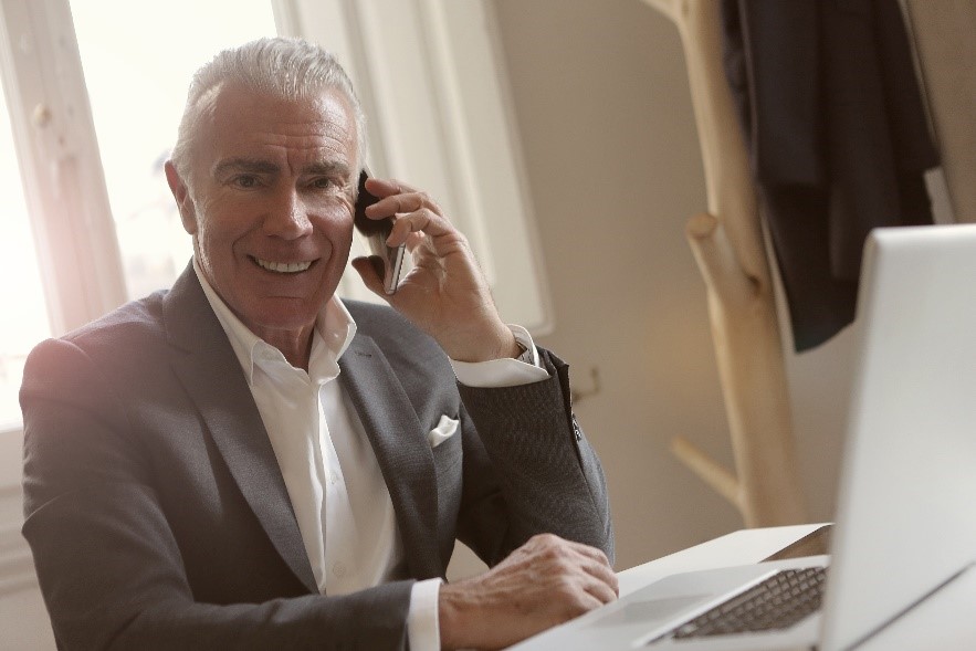 A man listening to a telephone in front of a laptop
